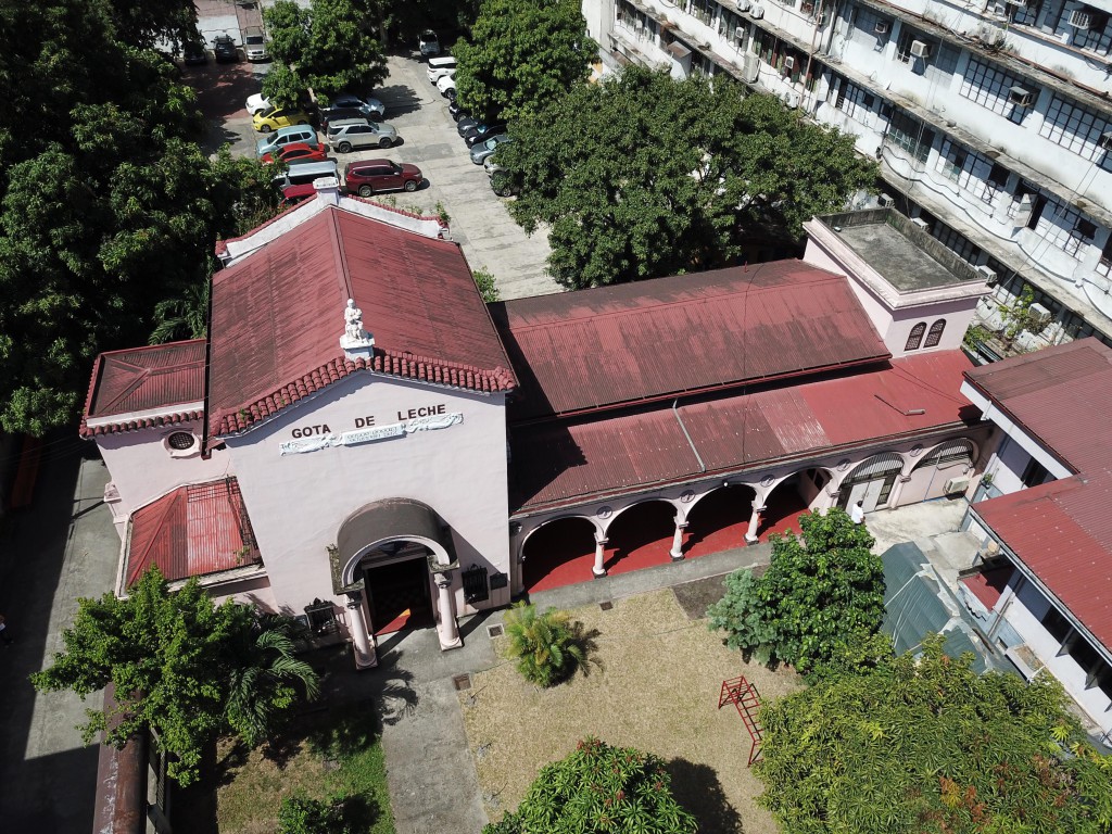 The building is surrounded by trees and has a vegetable garden in front